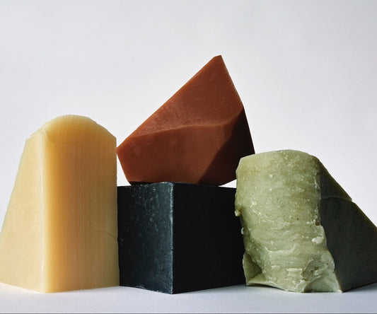 Stack of handmade bar soaps: charcoal soap, pink clay soap, green clay soap, rosemary soap